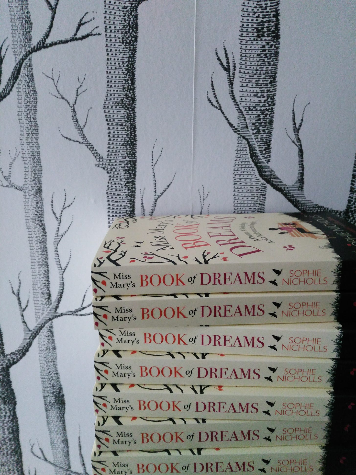 Stack of books by Sophie Nicholls. Books are the novel Miss Mary's Book of Dreams and are in front of wallpaper with black and white woodland tree pattern