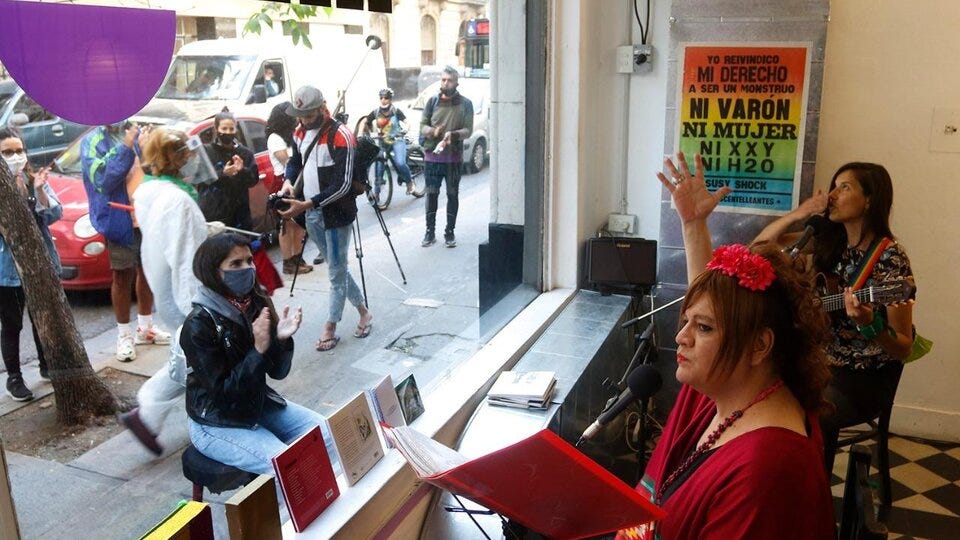 Susy Shock, vestita di rosso e con una rosa rossa tra i capelli, canta seduta di fronte alla finestra del teatro: dal lato della strada, una persona seduta su uno sgabello la applaude.