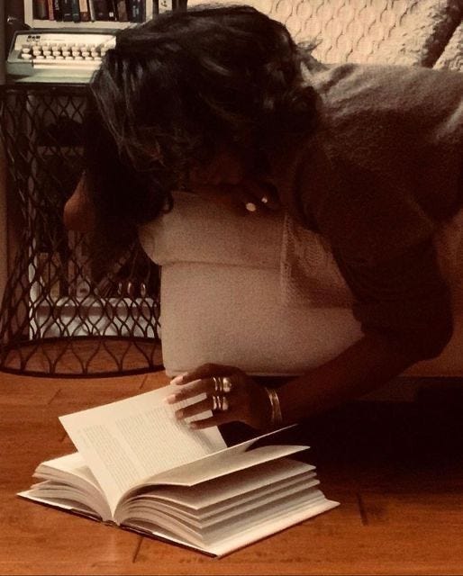 This may contain: a woman laying on the floor with her head in a pillow and reading a book