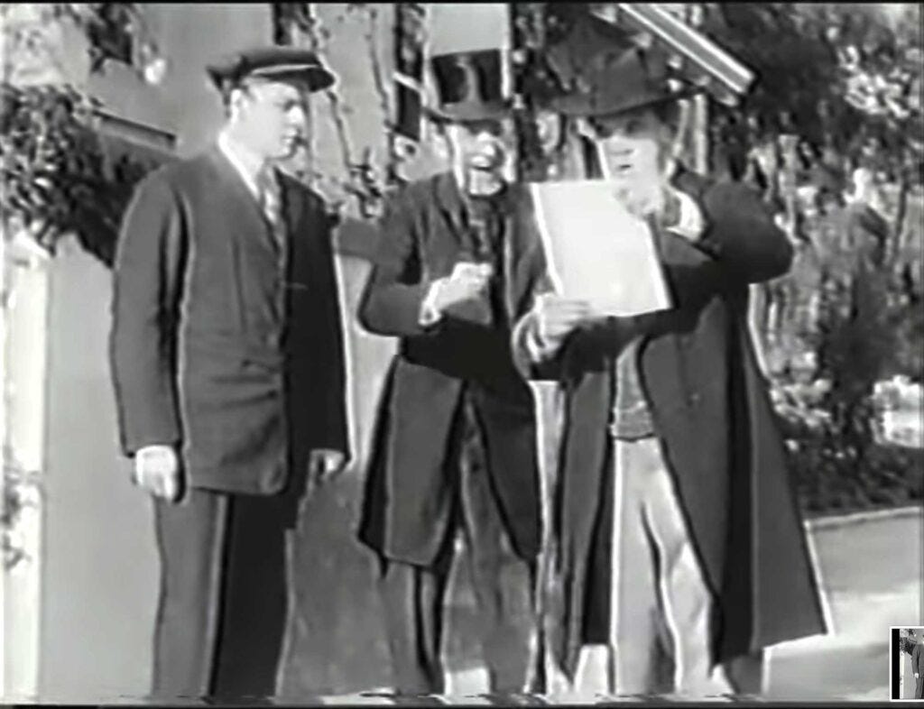 Three male characters from 1914 film Tess of the Storm Country, including, at right, the film's villain, a miserable capitalist called Deacon Elias Graves, who is joyfully reading the text of a law he's just had passed that will make life harder for the landless squatters on his beach-front land
