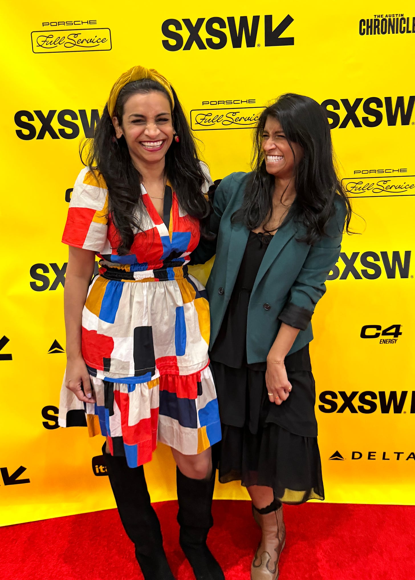 Two women, sisters, hug each other and laugh while posing in front of a yellow SXSW step and repeat background.