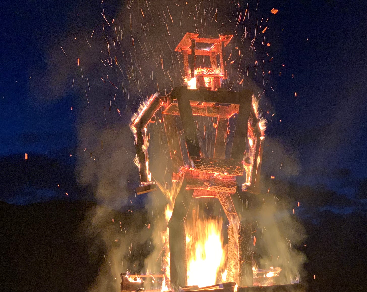 A burning man built of wood, sparks flying across a deep blue night