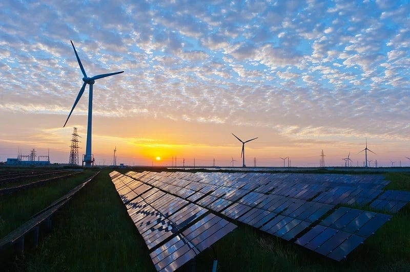 Landscape photo of solar panels and wind farm at sunrise (or maybe sunset) under scattered clouds