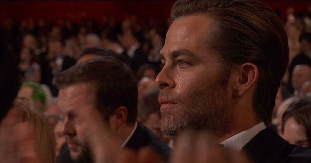 Chris Pine clapping with tears streaming down his face and a stoic expression in the audience at the Academy Awards.