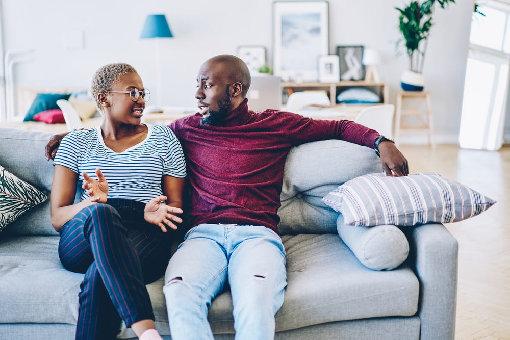 Young black man and woman talking on a grey couch