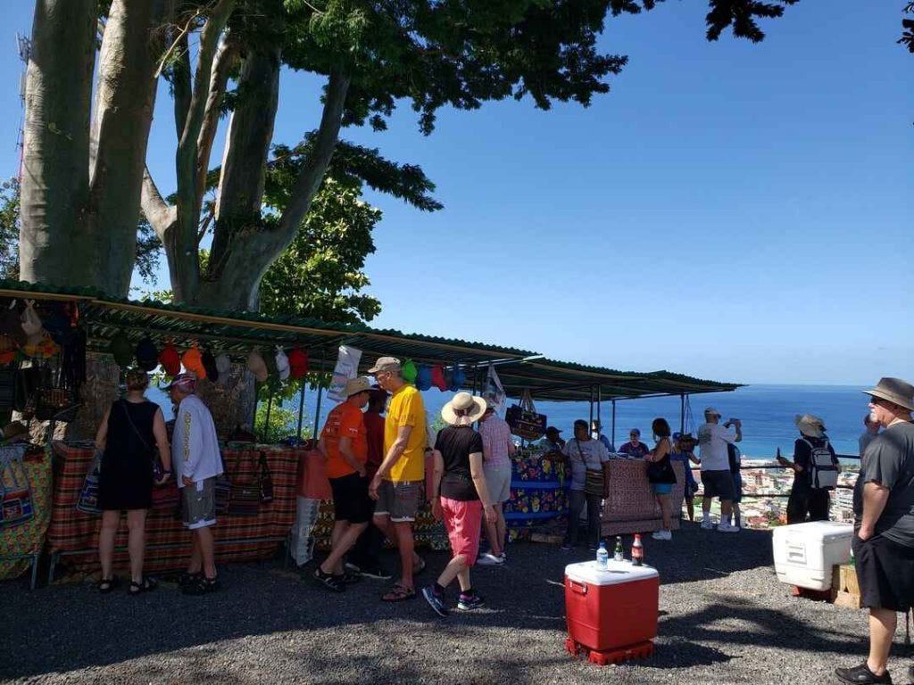 a group of people shopping at an open air marjet at the top of Bruce Morne in Dominica. The ocean is in the background