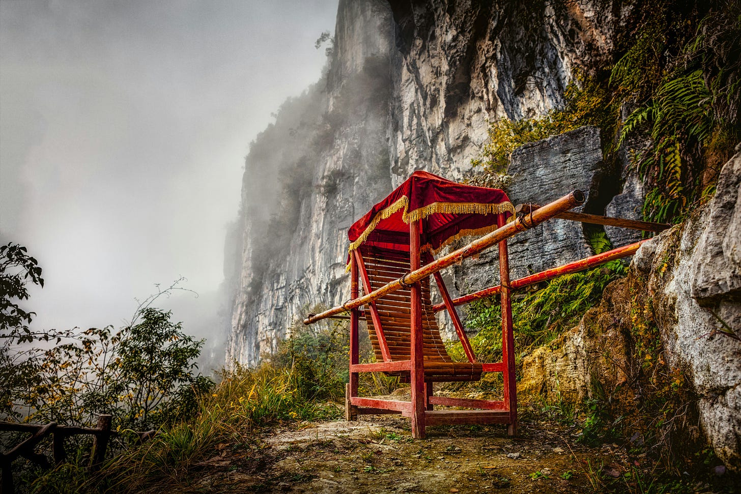 an empty reddish orange sedan chair, looking like its halfway up a rocky, misty, mountainside