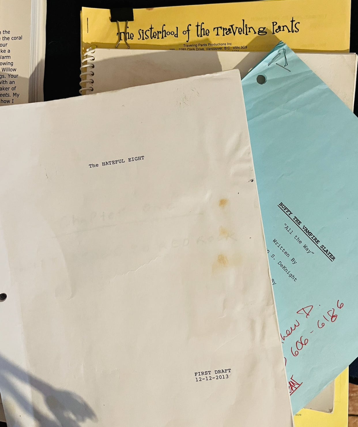 A stack of old scripts. Visible titles on the scripts are "The Hateful Eight," "Buffy the Vampire Slayer," and "The Sisterhood of the Traveling Pants."