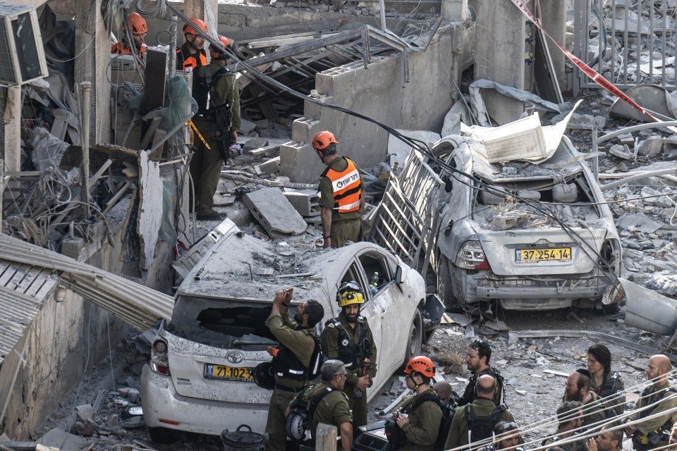 Israeli rescue teams searching for survivors amidst damaged buildings and cars following a missile attack.