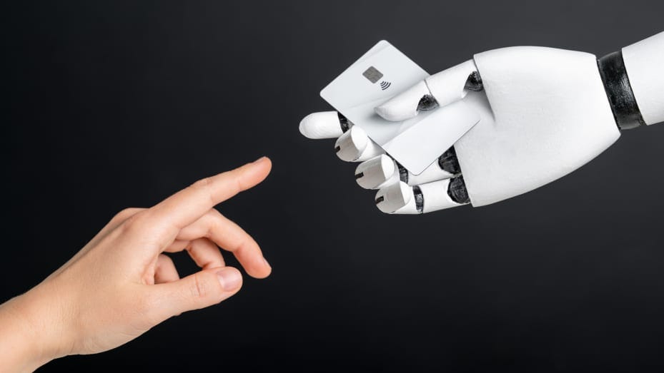 Human-like black and white robot hand holding plastic credit or debit card and human hand on black background. AI and finance concept