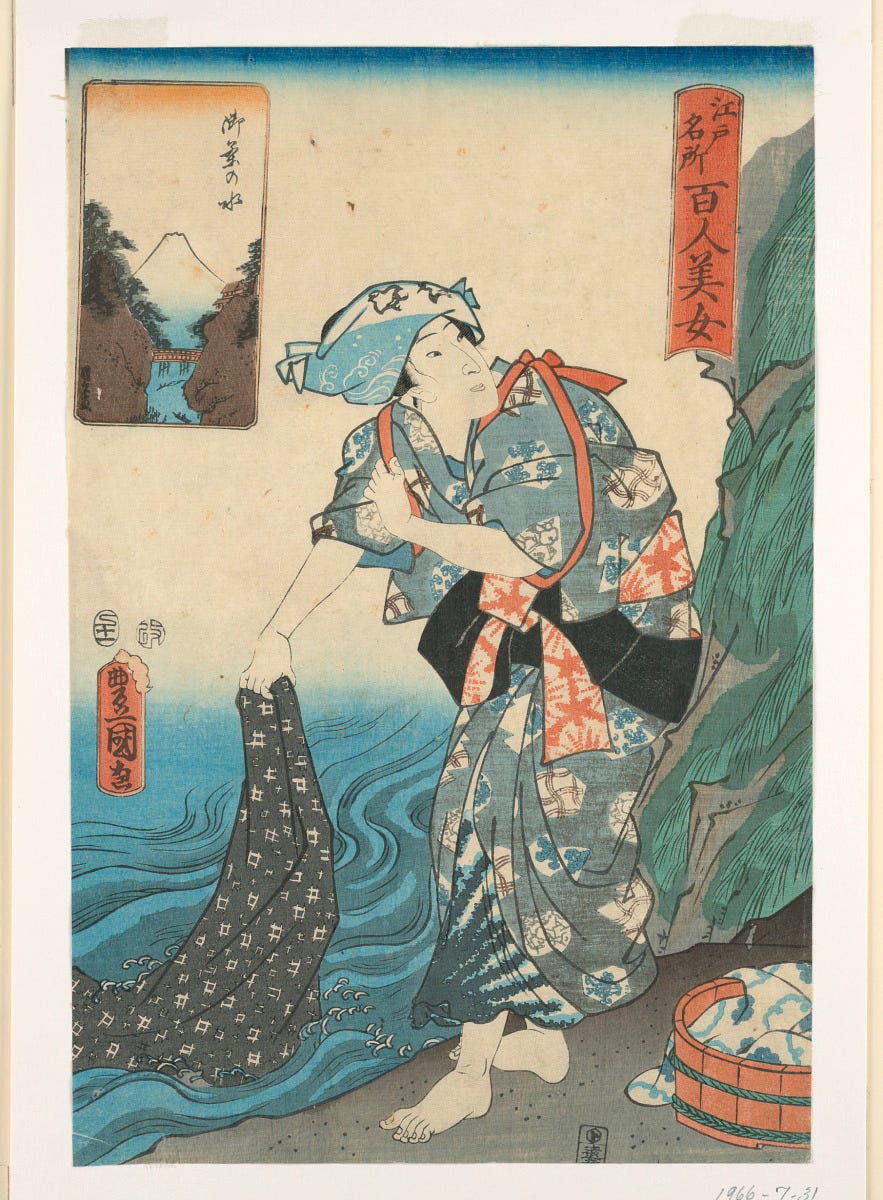 A barefoot woman in a patterned blue kimono stands at a riverbank, dipping a dark cloth into the flowing water. She appears to be engaged in washing fabric, with a basket of similar cloth nearby. In the top left corner, a small inset shows Mount Fuji framed by trees and a bridge. A barefoot woman in a patterned blue kimono stands at a riverbank, dipping a dark cloth into the flowing water. She appears to be engaged in washing fabric, with a basket of similar cloth nearby. In the top left corner, a small inset shows Mount Fuji framed by trees and a bridge.
