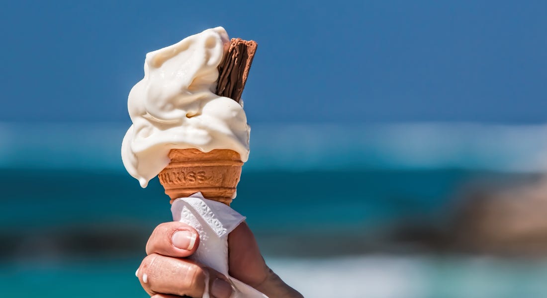 A vanilla whipped ice cream being held by a hand, with water in the background