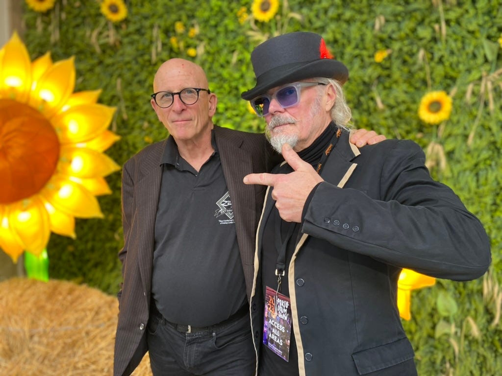 Man with top hat with a nother man standing in front of sunflowers