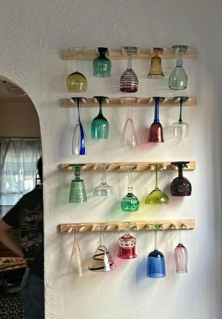 This may contain: there are many different colored glass vases on the wall and hanging from wooden shelves