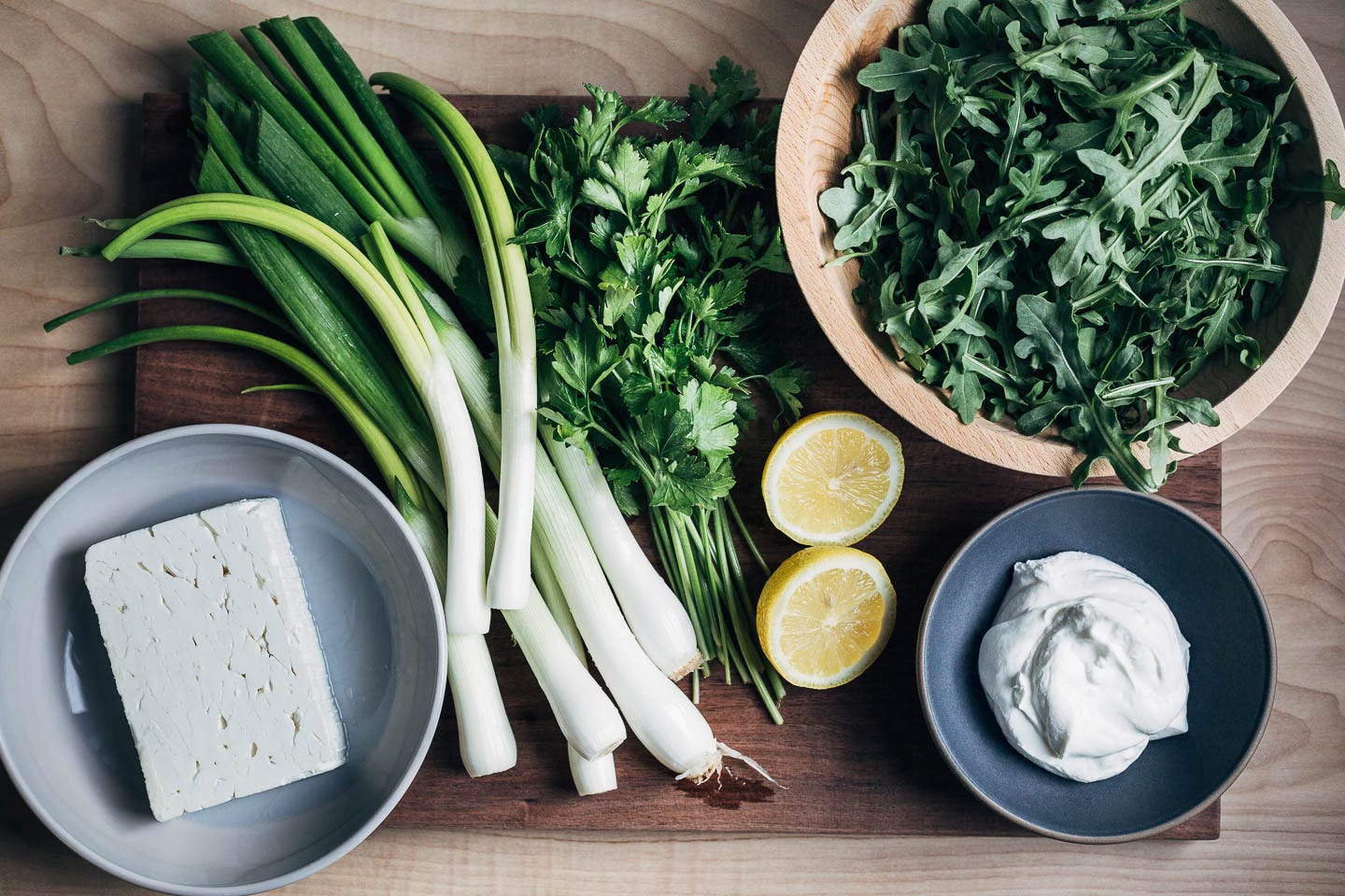 A cutting board with spring onions, feta, and other feta sauce ingredients. 