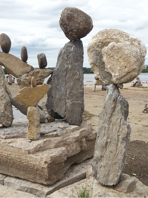 Rough hewn rocks balanced as inuksuit on a shoreline under a cloudy sky.