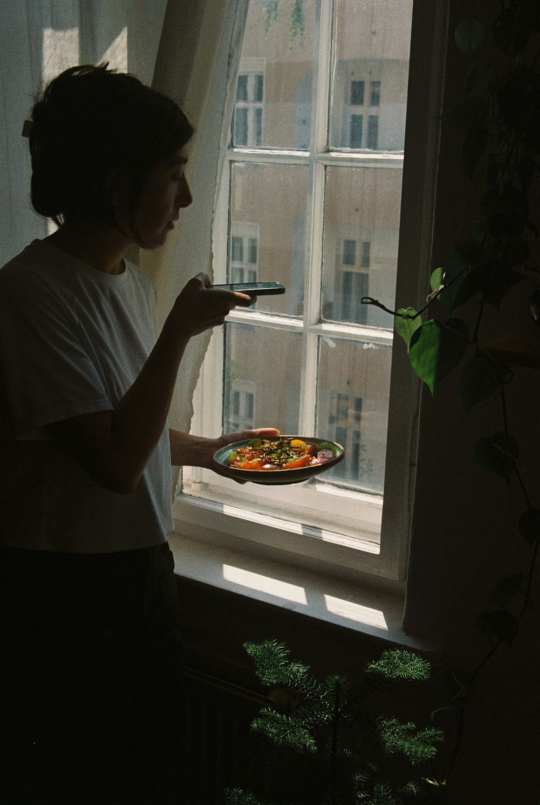 Devan by the window holding a plate of food while taking a picture.