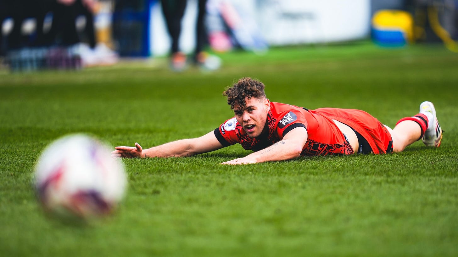 Huddersfield Town player Dion Charles slides on his front in the background, eyes fixed on a blurred ball in the foreground.