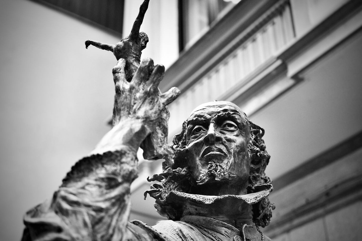 A black and white photo of a statue of a sculpter holding a crucifix he had made to inspect it. His eyes look keenly on the small figure.