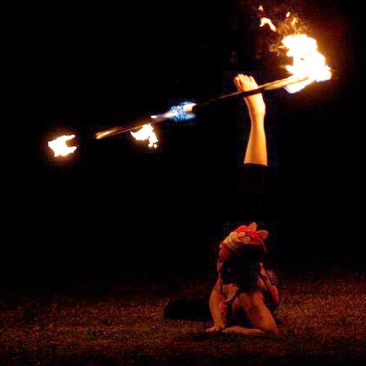 Photo of Lyric spinning a fire hoop on their ankle, wearing a pink cheshire cat hat