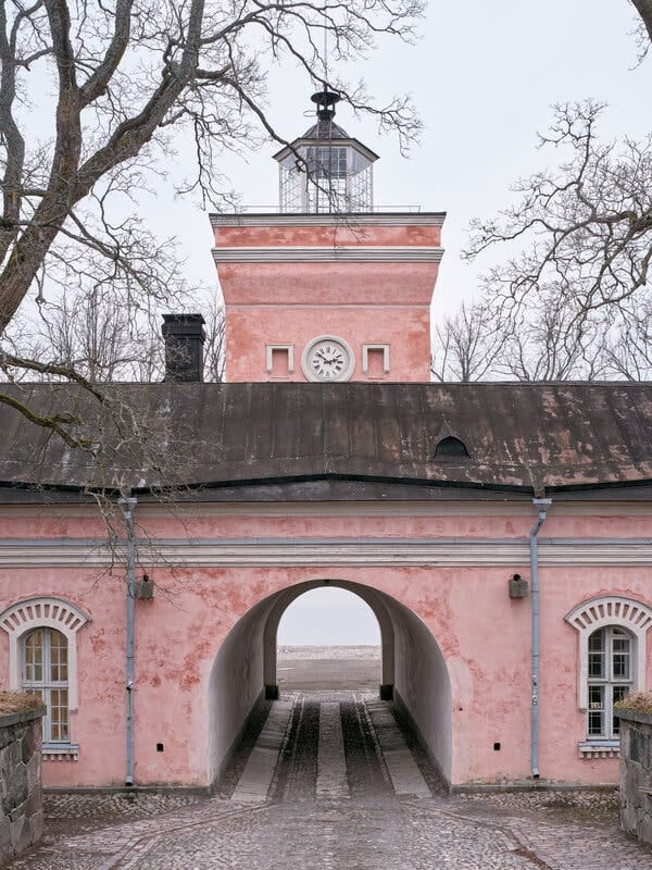 A pink building with an archway leading to water.
