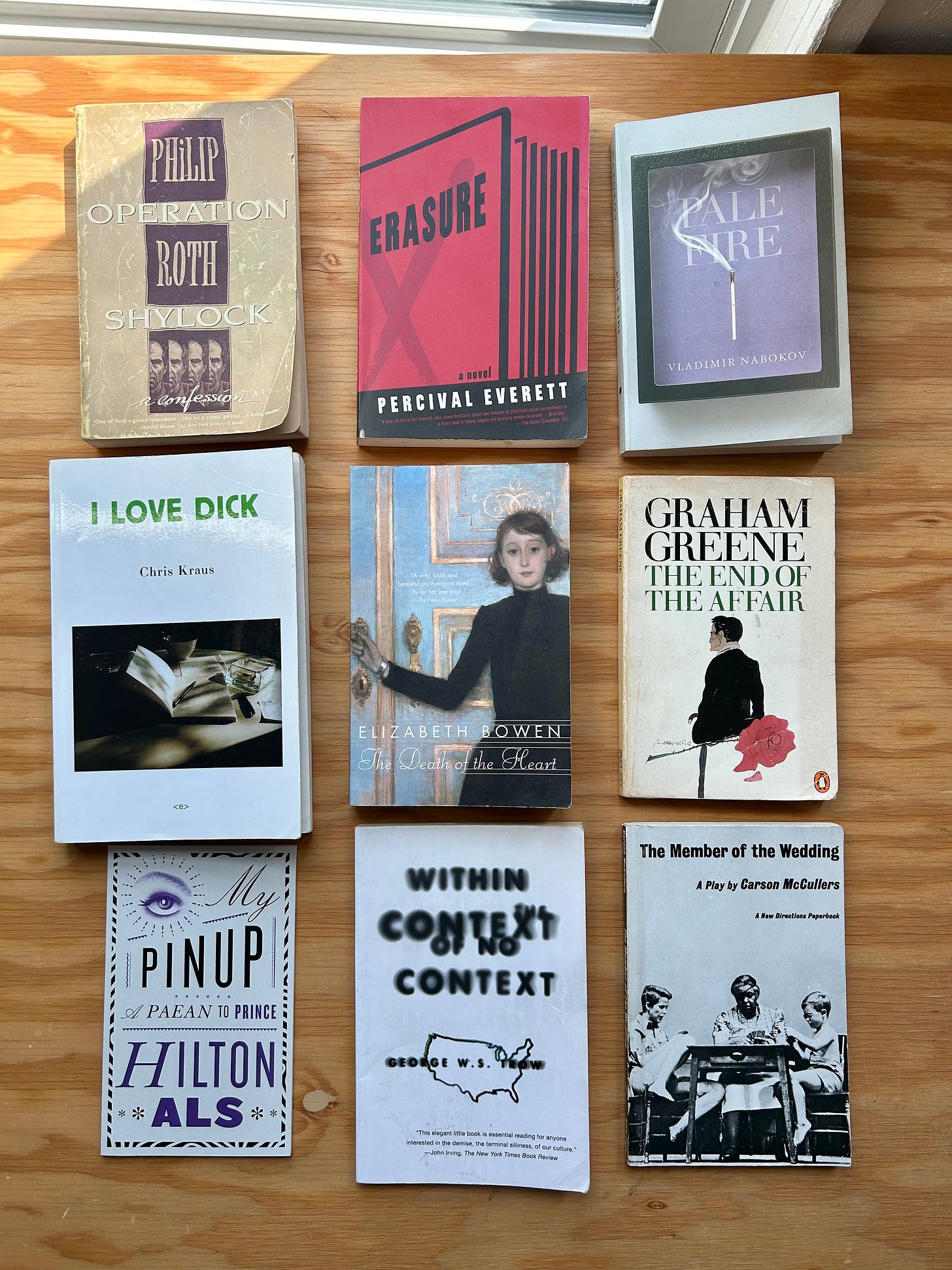 Image of 9 books laid flat on a wood surface. The books are:  “Operation Shylock: A Confession” by Phillip Roth “Erasure” by Percival Everett “Pale Fire” by Vladimir Nabokov “I Love Dick” by Chris Kraus “The Death of the Heart” by Elizabeth Bown  “The End of the Affair” by Graham Greene “My Pinup: A Paean to Prince” by Hilton Als “Within the Context of No Context” by George W. S. Trow “The Member of the Wedding” by Carson McCullers