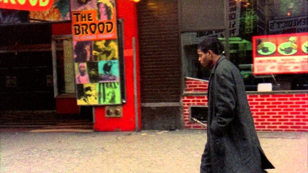 Movie still from Downtown 81. Jean-Michel Basquiat walks through the streets of New York City, passing by a movie theater and a restaurant
