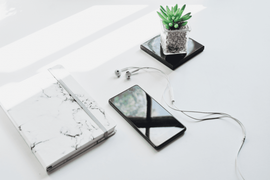 made with mindful productivity in mind - notebook, cell phone, earbuds and small plant on white desktop