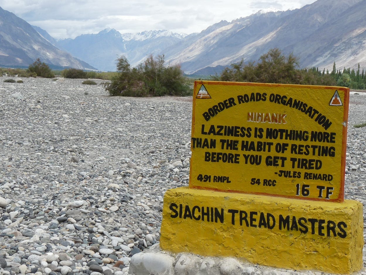 A road sign created by Project HIMANK that reads, “laziness is nothing more than the habit of resting before you get tired.”