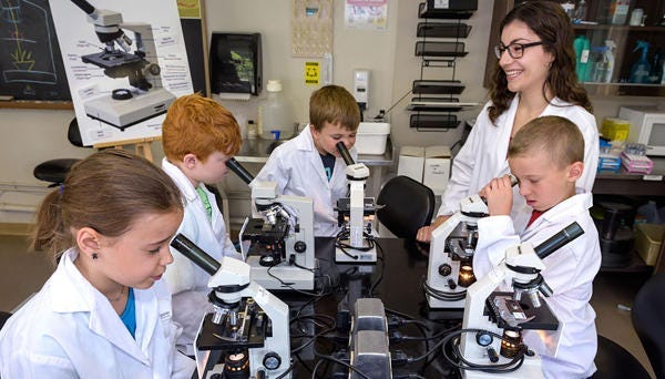 teacher and students in lab coats looking at microscopes