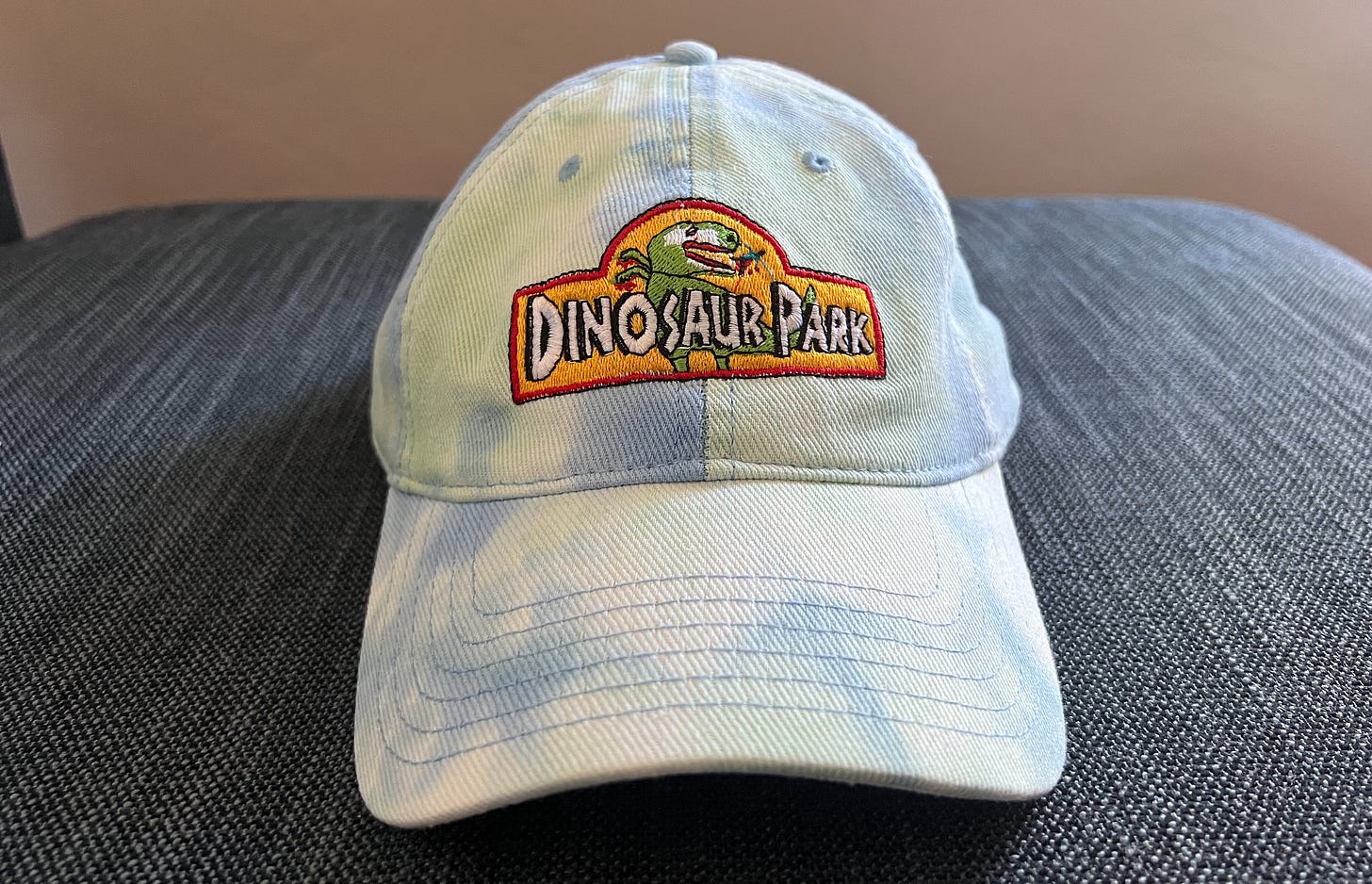 Tie die blue cap with DINOSAUR PARK logo on it, as dinosaur eats human