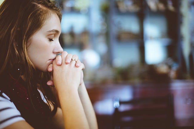 A young woman kneels with her fingers intertwined and her eyes closed