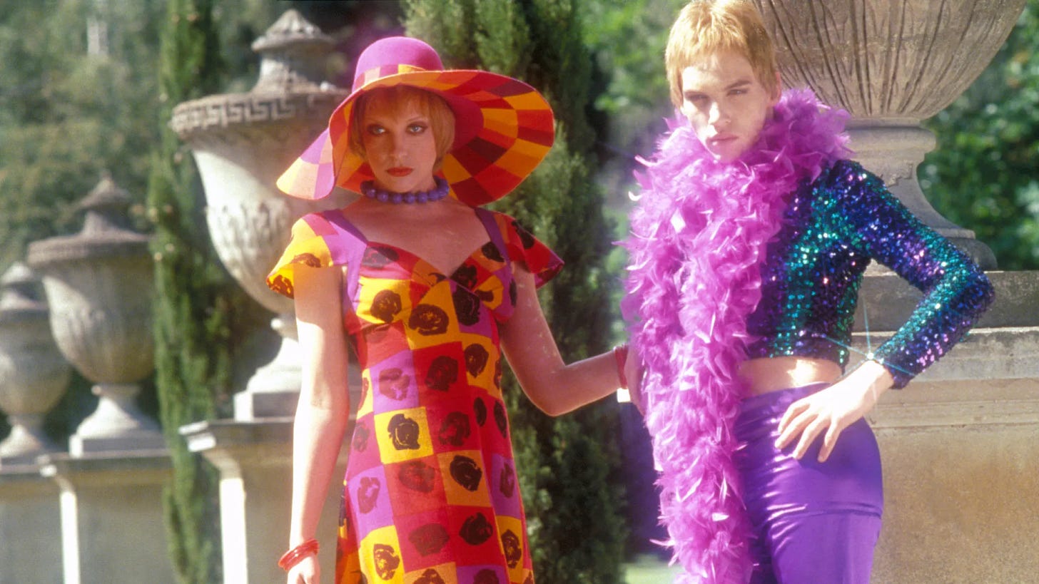  Jonathan Rhys Meyers & Toni Collette in a sparkly purple outfit & purple feather boa and a pink/yellow dress with matching hat, respectively, in Velvet Goldmine. 