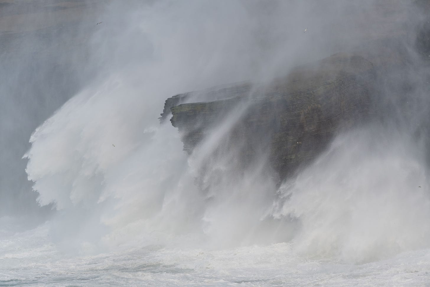 Huge waves crashing over tall cliffs with clouds of seaspray