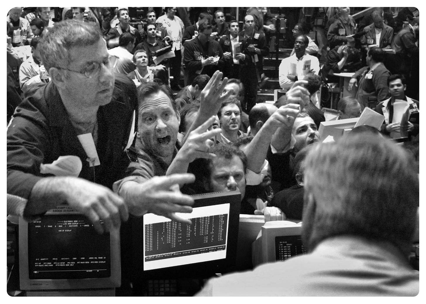 A black & white photo from the 1980's, found under google image search results 'Wall Street Bull Market'. Depicts many people on a chicago trading room floor, in the midst of trading. Gives a sense of frenzy