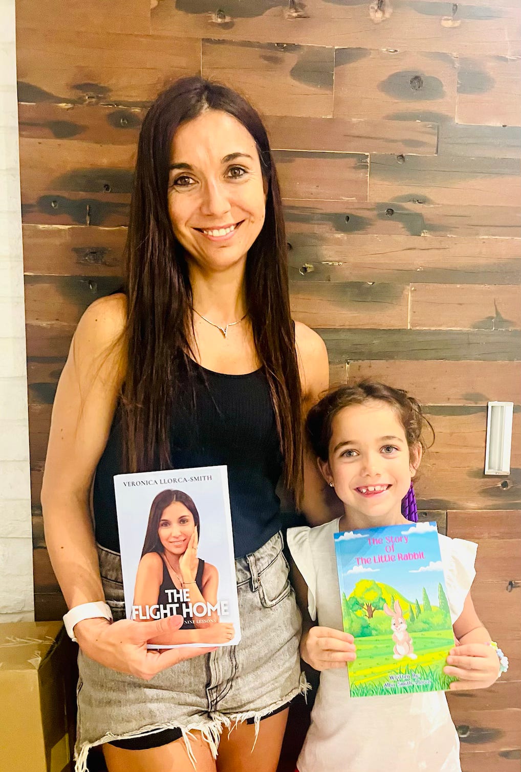 Picture of myself with a black top holding my book and Alba, a 6-year old holding her book. Both smiling at the camera. 