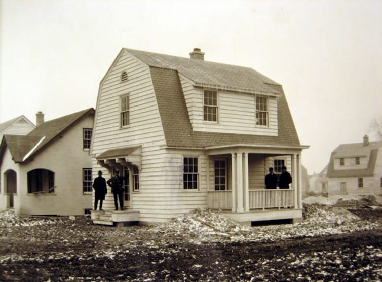 Sepia-toned photograph of a group of men standing in front of a newly-built house. Sepia-toned photograph of a group of men standing in front of a newly-built house.