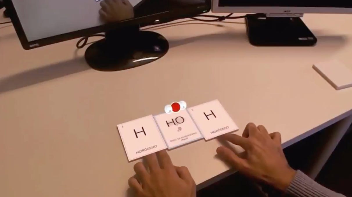 Someone places cards next to each other with H, HO, and H on them. In the augmented reality display, we see those compounds come together and form into H2O.