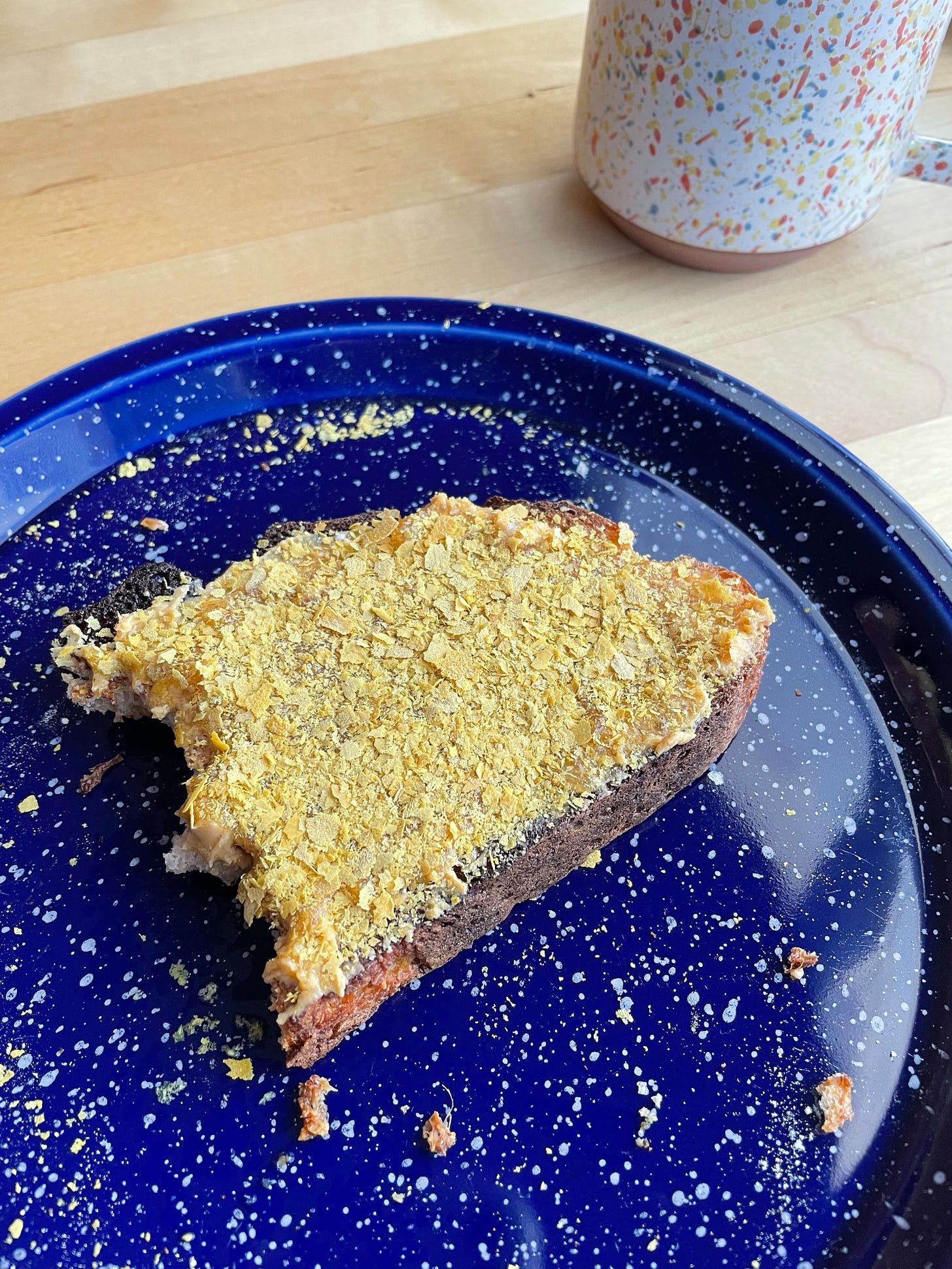 Sourdough toast with peanut butter, honey, flaky sea salt and nutritional yeast. A cup of coffee nearby.