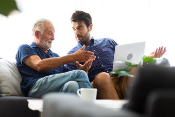 Father and son family time together at home concept. Smiling old father and happy son sitting on sofa using digital laptop computer in living room at home