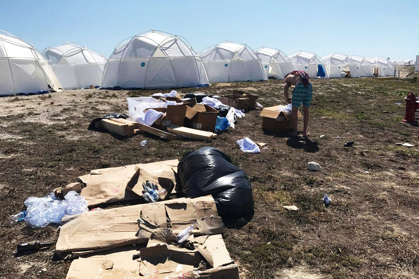 A group of white geodesic domes surrounded by garbage with a man picking through the tash.