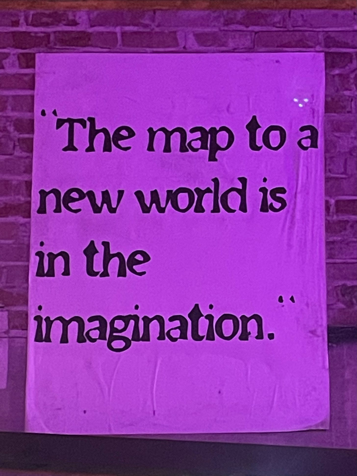 A sign on a brick wall, reading "The map to a new world is in the imagination."