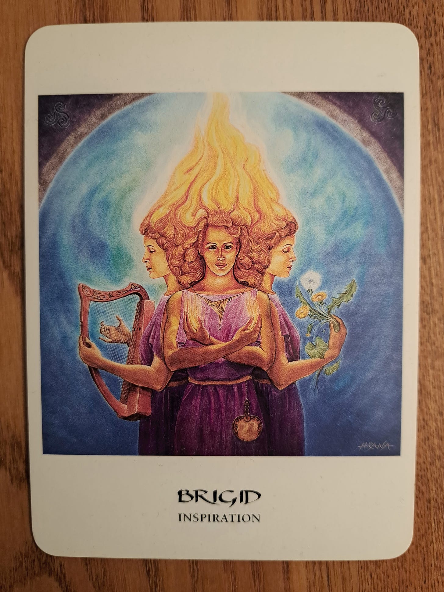 Brigid oracle card showing 3 fiery-haired goddesses holding a harp, fire, and flowers