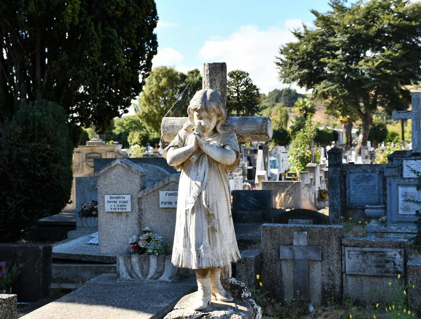 Graveyard with angel statue in front of a cross. 