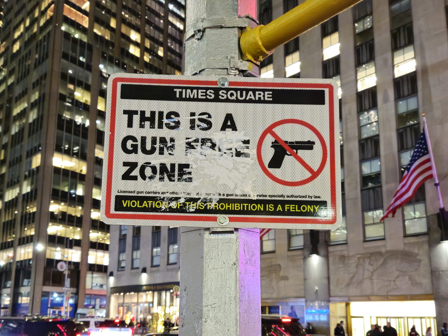 A sign that says Times Square, This is a Gun Free Zone, and Violation of this Prohibition is a Felony. There is also an image of a gun inside a red circle with a line crossed through it.