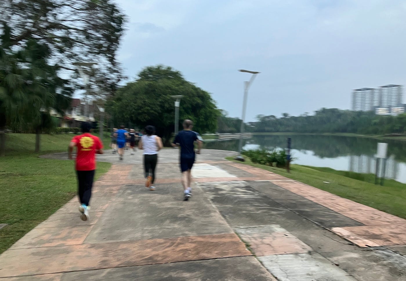 Runners on a wide paved path, next to the river and trimmed grass