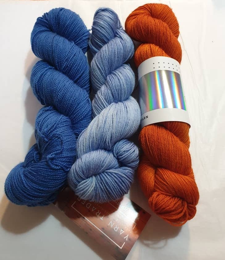 Yarn Trader Studio Skinny Sock Yarn from left to right Electric City (electric blue color), Caladan Waters (sky blue color), Hedgehog Fibers Burnt Orange yarn.