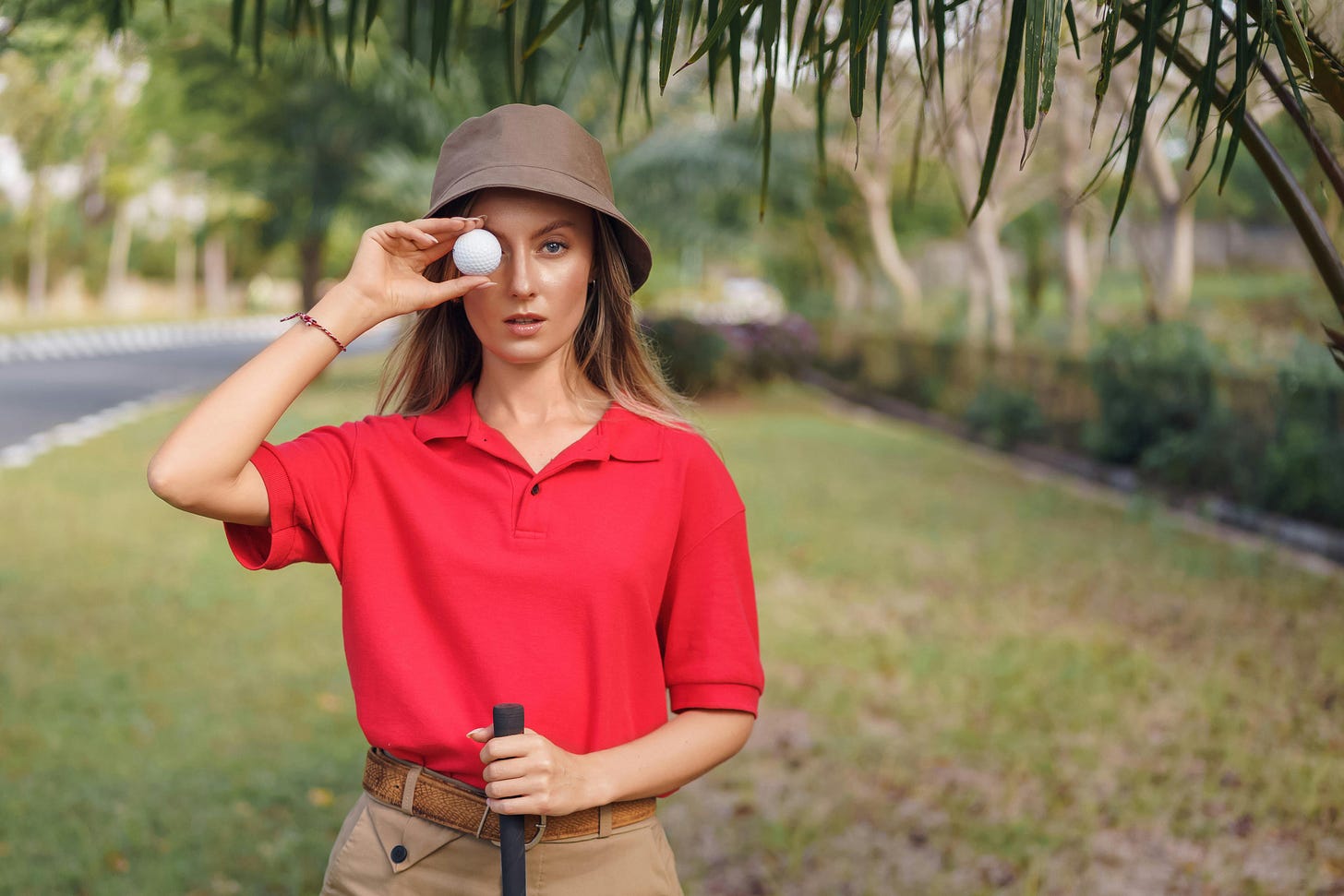 Woman in orange golf shirt with golf ball against eye