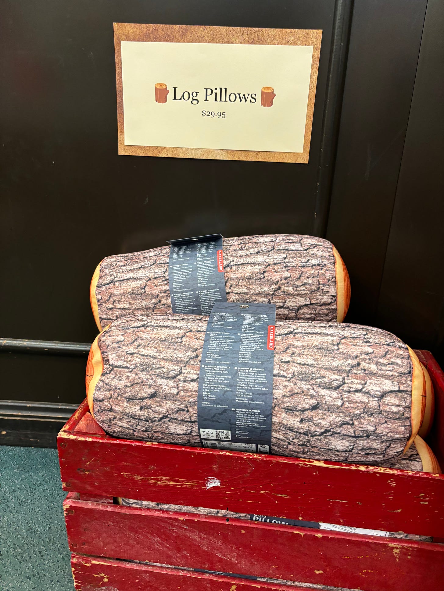 Two brown-bark-patterned pillows shaped like logs in a red wooden box.