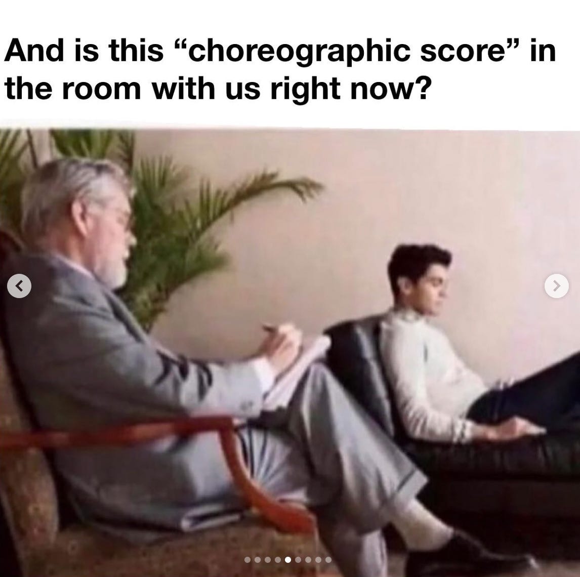 a classic image of a therapy session, featuring two white men. the older one is the therapist, asking the younger man, "And is this "choreographic score" in the room with us right now?